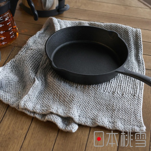 日本桃雪SEK抗菌防臭檜木鬆餅紋毛巾，放置在灰色紋理毛巾上，旁邊有一個黑色鑄鐵鍋。