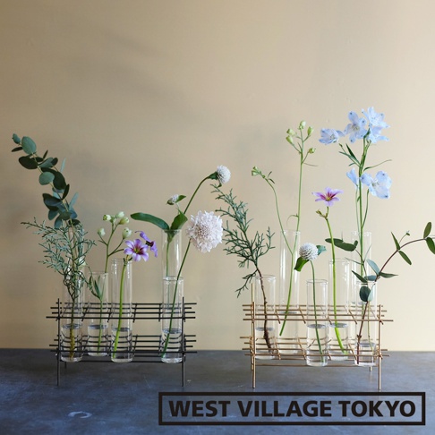 兩個金屬支架，分別裝有玻璃花器。左側為黑色金屬支架，內有六個玻璃管，插著綠葉、紫色小花、白色圓形花和綠色枝條。右側為金色金屬支架，內有六個玻璃管，插著淡紫色花、藍色花、白色小花和綠葉。