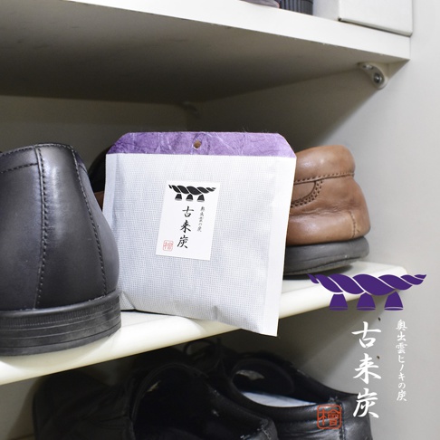 一個白色帶有紫色頂部的包裝，上面印有「古來炭」字樣的調濕木炭包，置於鞋架上，旁邊有黑色和棕色的鞋子。
