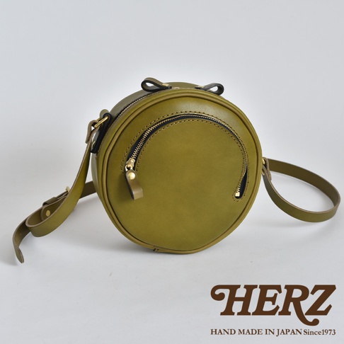 橄欖綠皮革圓形手提包，配有雙拉鍊開合、可調式肩帶和頂部提把。