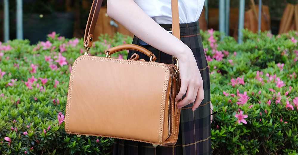 棕色皮革手提斜背包，方形設計，有頂部提把與可拆卸肩帶，精緻車縫線裝飾。