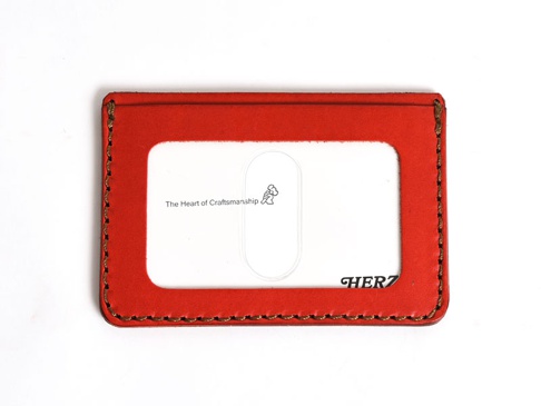 職人手作皮革橫式票券收納夾，紅色皮革，邊緣縫線為咖啡色，正面有一個透明視窗，可見「The Heart of Craftsmanship」字樣及品牌標誌。