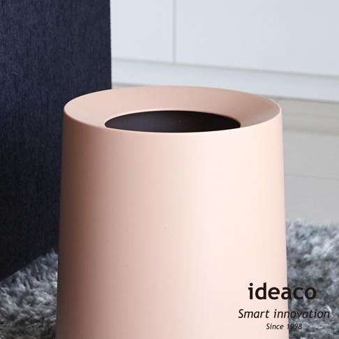 一個淺粉色的圓形垃圾桶，具有簡潔的設計和寬大的開口，內側為黑色。