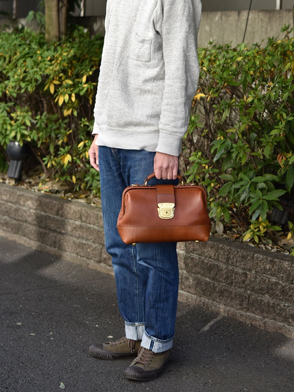 棕色皮革製成、帶有金色鎖扣的迷你口金單肩包，由手提或肩背方式展示。