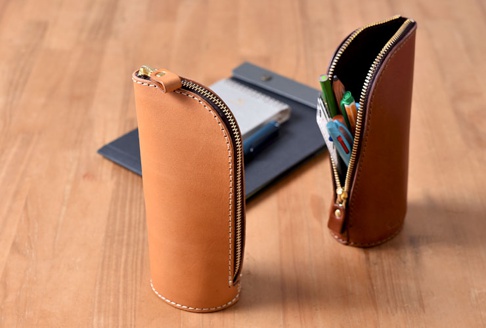 兩款職人手作皮革直立式收納筆袋，一款為淺棕色，另一款為深棕色。兩者均採用拉鍊開合，內有各式筆類。