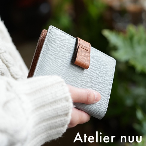 Atelier nuu 品牌 logo，淺藍色皮革雙折短夾，由手持展示，細節處搭配棕色皮革。