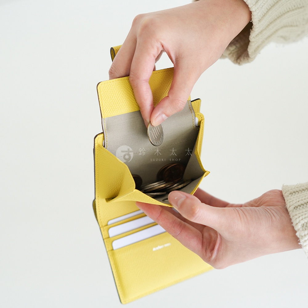 Atelier nuu noble 短夾，黃色皮革材質，兩手正在放入銅板，內有卡片層。