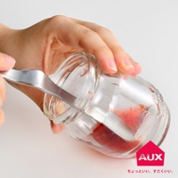 手持金屬果醬抹刀，正在從裝有紅色果醬的透明玻璃罐中取出果醬。