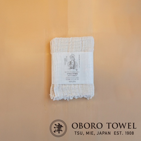 一條米白色三層紗純棉戶外掛脖毛巾，帶有手繪圖案包裝紙，標有日文文字。