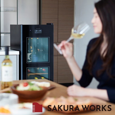 黑色 SA38 雙溫酒櫃，有兩層玻璃門，內部展示多瓶酒類。上方顯示溫度 0℃ 和 14℃。酒櫃置於廚房檯面上，左側有一瓶白酒，右側有一位女士手持酒杯。