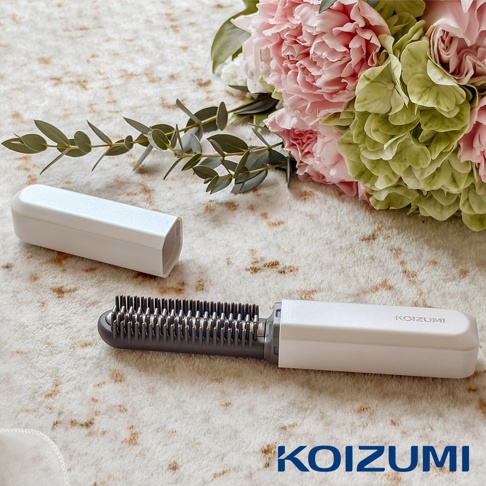 KOIZUMI 迷你瀏海梳，白色機身搭配灰色梳齒，旁邊擺放著粉色與綠色的花束，以及其白色收納蓋。