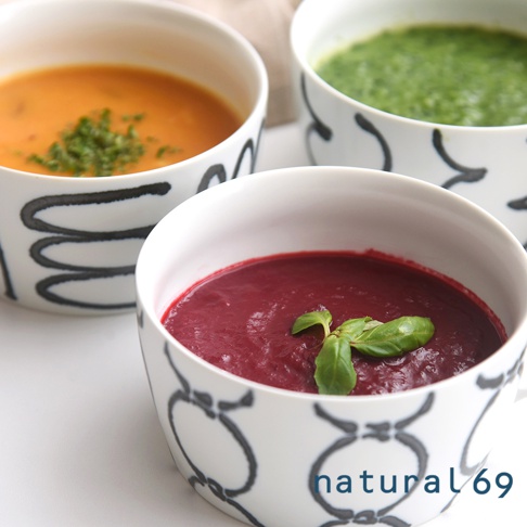 三碗陶瓷湯杯，分別盛裝橘黃色、綠色和紫紅色濃湯，湯杯外側有黑白相間的手繪圖案，其中一碗湯上裝飾著綠色羅勒葉。