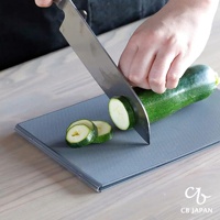 CB JAPAN logo 標誌下的深灰色可折疊砧板上，一只手正用刀切一片櫛瓜。