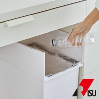 一只手將空塑膠瓶放入白色對開分類垃圾桶內，垃圾桶藏於廚櫃下方。