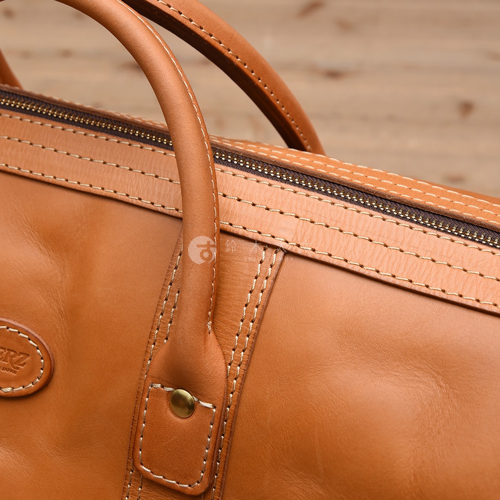 職人手作皮革肩背手提拉鍊波士頓包，採用光滑棕色皮革製成，配有雙提把、拉鍊封口及精緻縫線裝飾，整體呈現簡約大方的風格。