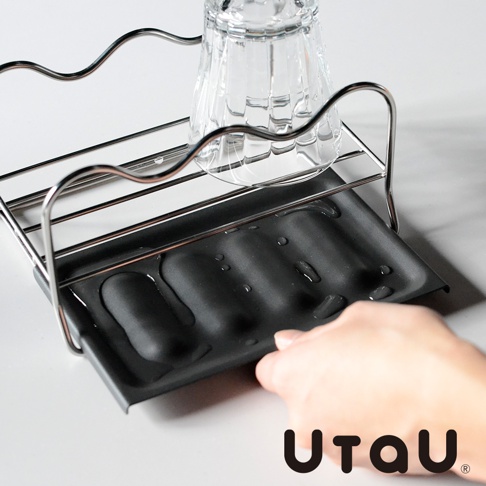 不鏽鋼多功能萬用瀝水支架，設有黑色集水盤，上方置有一個玻璃杯，手部正將集水盤拉出。