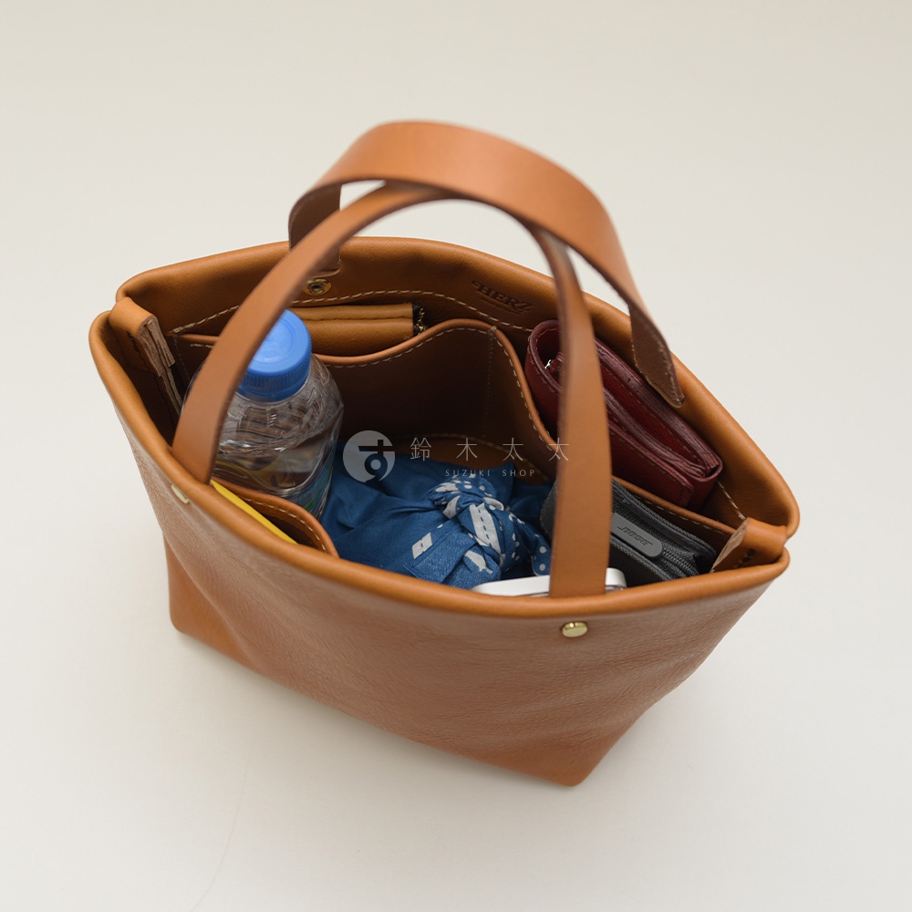 簡約棕褐色皮革托特包，內有水瓶、藍色布包、紅色皮夾和手機。包包有兩個提把，內部隔層清晰，材質為皮革。