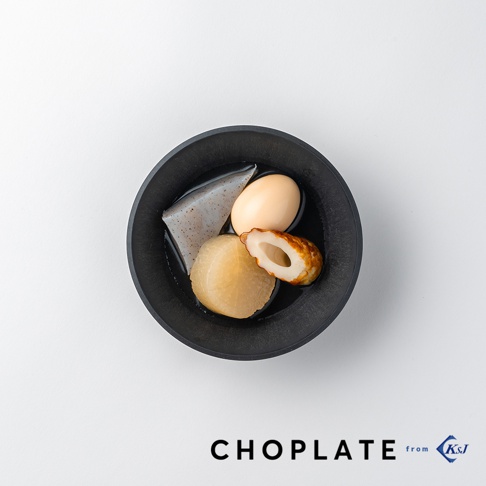 黑色CHOPLATE沙拉碗盛有日式關東煮，包含一顆水煮蛋、一塊蘿蔔、一片魚板及一塊三角形的蒟蒻，碗內有湯汁，整體呈現精緻的日式料理風格。
