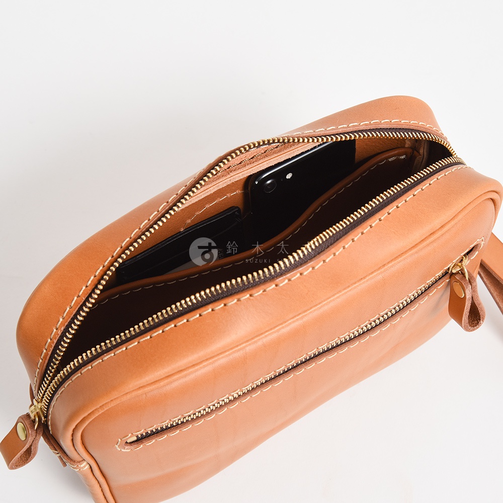 淺棕色皮革手提包，拉鍊開口，內有手機及卡片夾。包包外部有拉鍊口袋，搭配金色拉鍊及縫線。