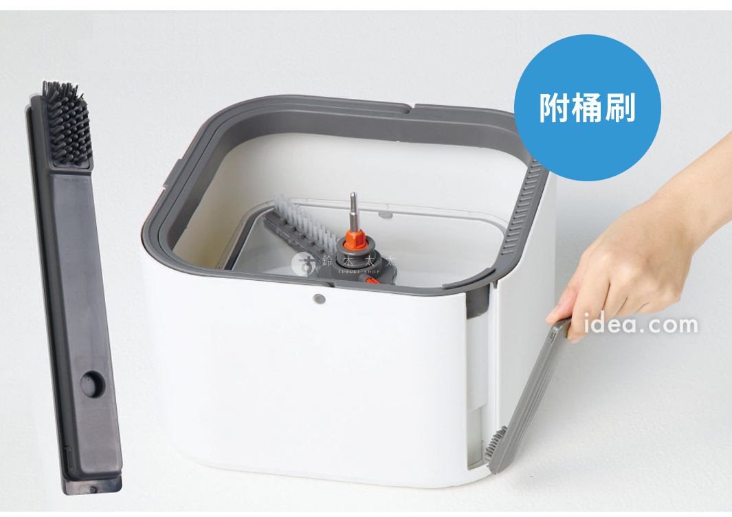 一個白色方形的清潔拖把專用桶，內部底部設有旋轉刷頭與中心軸，一隻手正在將隨附的灰色長條狀清潔桶刷插入桶身側邊的收納槽中，畫面左側亦展示該桶刷的細節。