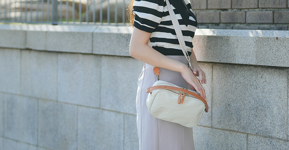 一位女性身穿黑白條紋上衣，斜揹著一個米白色斜背包，包包上有皮革飾邊。
