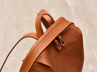 職人手作皮革後背包，採用溫暖的棕褐色，展現天然皮革的細緻紋理與簡約褶皺設計。雙拉鍊頭設計，搭配堅固的縫線，強調細節與質感。