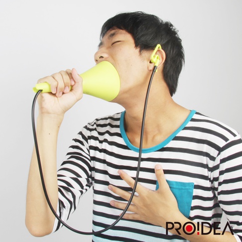 一位男子正使用一個淺綠色的喇叭狀消音高歌器，該高歌器連接有黑色線材與耳機。男子身穿一件黑白條紋的長袖上衣，左耳戴著一個黃色的耳機。