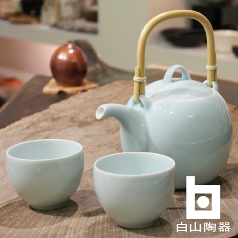 淡藍色陶瓷壺搭配竹製提把，壺旁擺放兩個同色系的茶杯，整體呈現簡約日式風格。