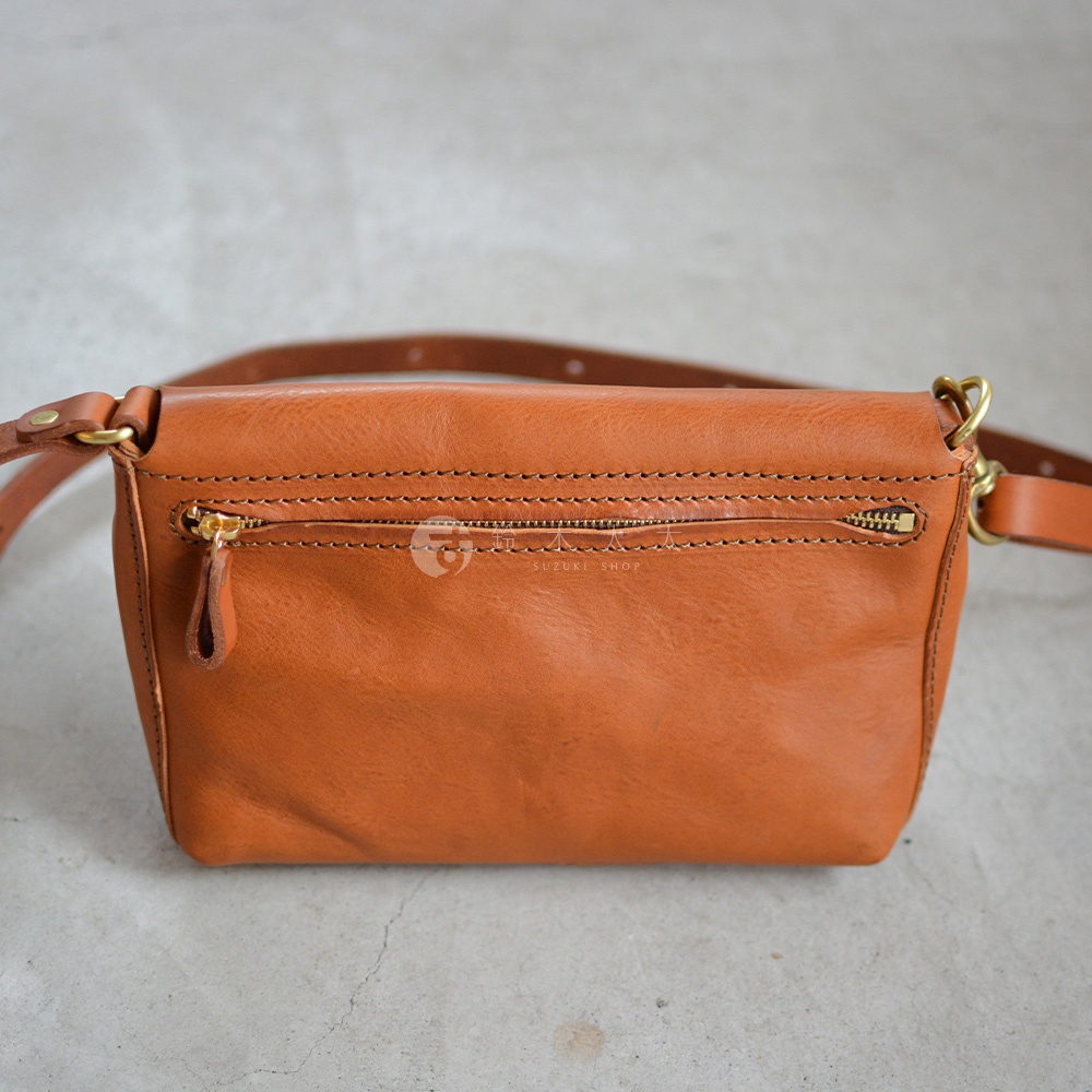 棕色皮革斜背包，正面有一個拉鍊口袋，搭配金色拉鍊和皮革拉環。