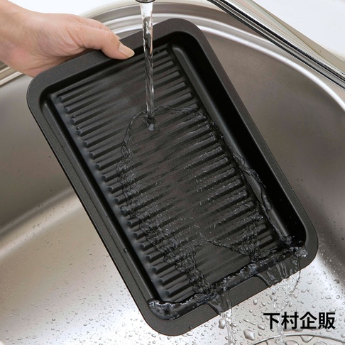 一個黑色、帶有波浪紋路的烤盤，正在水槽中被水沖洗，烤盤邊緣有滴水。