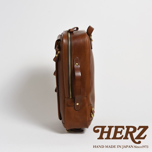 棕色皮革製成的兩用後背包，側面展示，配有金色拉鍊和扣環，以及提把。