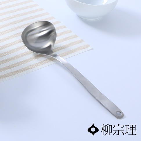 銀色不鏽鋼湯杓，勺頭有波浪紋理，長柄末端有掛孔，放置於淺色條紋餐墊上。