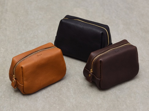 職人手作皮革Organ拉鍊收納包，共三色：淺棕色、深棕色、黑色。包身為荔枝紋皮革材質，配有金色拉鍊和同色系皮革拉環，底部與側邊有縫線細節。