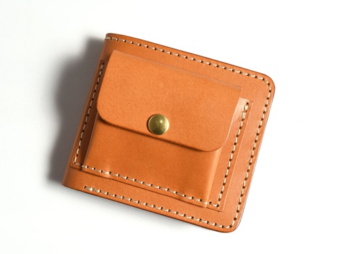 淺棕色皮革製成的雙折短夾，外附一個帶有黃銅按扣的零錢袋，邊緣以白色縫線手工縫製。