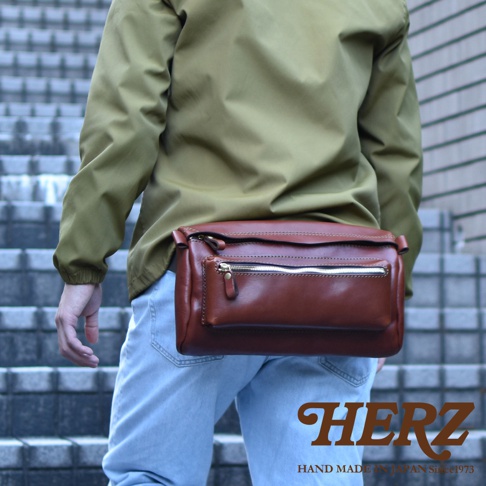 棕色皮革製成的兩用腰掛斜背包，包身結構飽滿，正面設有拉鍊主袋和一個外置拉鍊小袋，手工縫線清晰可見。