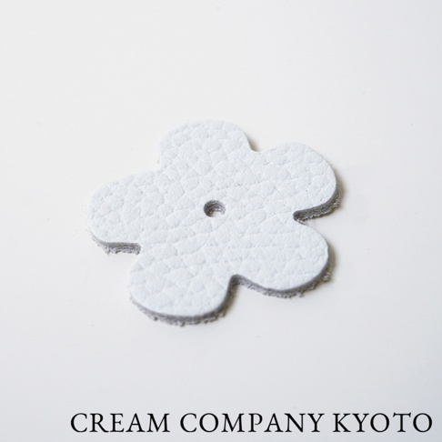 淺灰色皮革製成的花朵形狀吊飾，帶有紋理和中央小孔。