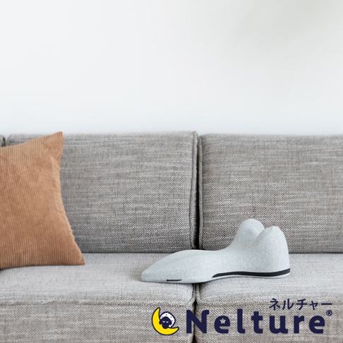 淺灰色布面肩頸背拉伸牽引枕，造型符合人體工學，兩側有弧形支撐，中間為凹陷設計，底部有黑色邊緣。