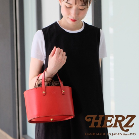 紅色皮革束口袋手提包，搭配咖啡色束口內袋，包包正面有金色旋轉鎖扣，兩側有提把，款式簡約，材質為皮革。