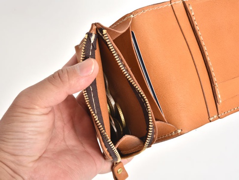 手持棕色皮革直式卡片收納雙折短夾，內有零錢袋裝有硬幣，以及卡片夾層。
