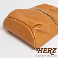 棕色皮革製成的大開口圓角後背包，帶有金色拉鍊，底部有金屬鉚釘，側面有品牌標誌。