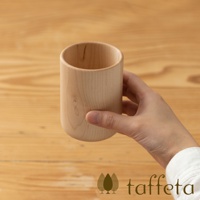 手持一個淺棕色楓木製水杯，杯身呈現天然木紋，底部為圓潤造型。