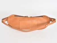 一個淺棕色的職人手作皮革斜背包，配有頂部拉鍊、前袋和可調節的皮革肩帶，整體設計簡潔。