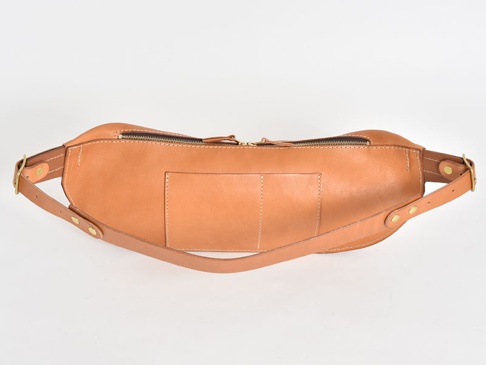 一個淺棕色的職人手作皮革斜背包，配有頂部拉鍊、前袋和可調節的皮革肩帶，整體設計簡潔。
