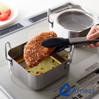 逸品物創不鏽鋼方型炸物鍋組，包含一個方形不鏽鋼炸鍋，鍋內有金黃色炸油，一塊裹滿麵包粉的炸物正由黑色夾子夾起，鍋的後方為另一組不鏽鋼炸鍋，鍋內放置濾油網。