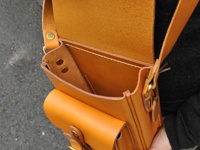 一件職人手作皮革皮扣直式單肩包，採用亮棕色皮革製成，包身有兩個前置口袋，以皮扣開合。