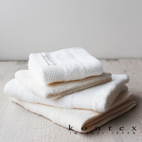 疊放的白色與米白色今治有機棉雙織浴巾，表面有鬆餅紋理，其中一條白色浴巾上帶有品牌標籤。