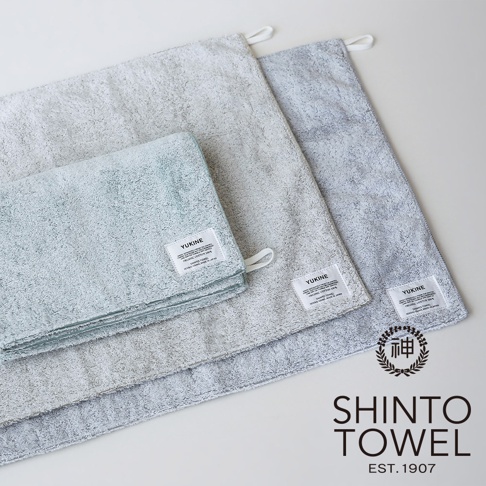 三條不同尺寸和顏色的柔軟毛巾，其中一條是淺藍色，另外兩條是淺灰色，都帶有品牌標籤。