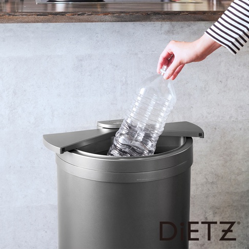 一個灰色的30公升大容量自動感應靜音垃圾桶，桶身呈圓柱形，配有銀灰色觸控蓋，一位女士正將一個裝有液體的透明塑膠瓶投入桶中。