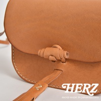 淺棕色皮革流蘇側背包，帶有獨特的皮革扭結開關設計，手工縫線清晰可見，簡約大方的款式，適合日常搭配。