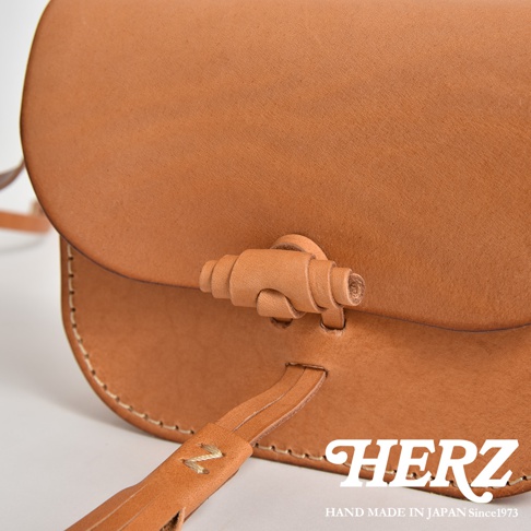 淺棕色皮革流蘇側背包，帶有獨特的皮革扭結開關設計，手工縫線清晰可見，簡約大方的款式，適合日常搭配。